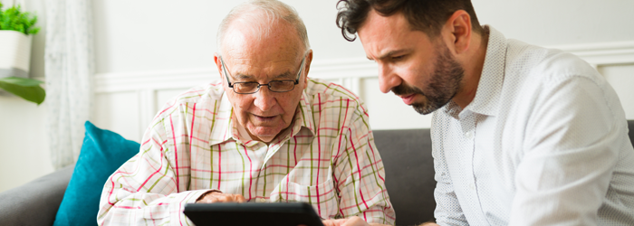 Adult man helping his elderly dad look at something on his tablet