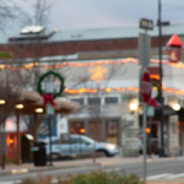 Out of focus car and business on small town streets intersection with branch of a Christmas tree visible