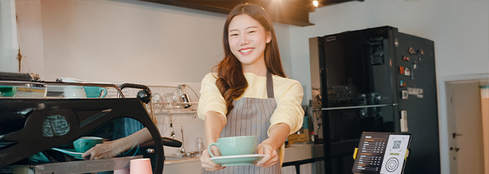 Young girl holding a coffee cup at her first job as a barista in a coffee shop