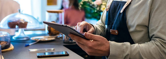 Man wearing apron and holding tablet while standing behind the counter of their bakery business