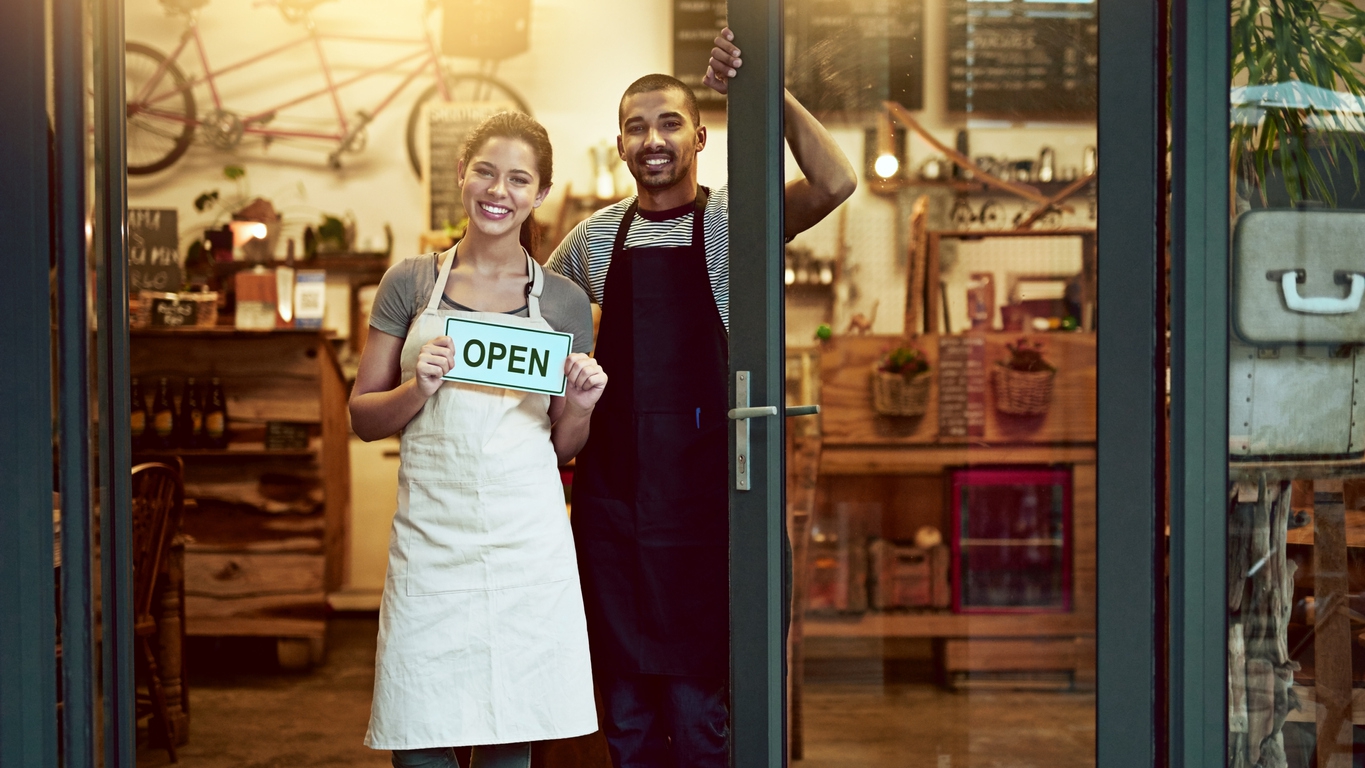male and female small business owners displaying open sign to show they're ready to accept customers