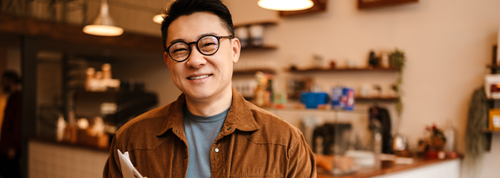 Male business owner holding clipboard and paperwork while smiling at his business