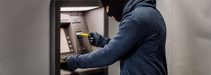 Person in hoodie and black mask skimming money at an ATM.