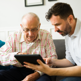 Adult man helping his elderly dad look at something on his tablet
