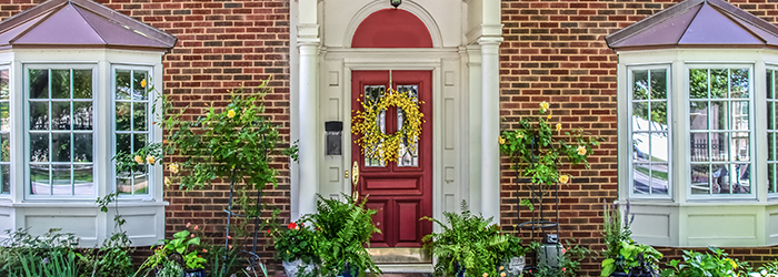 Front door and front exterior of a brick home with bay windows and greenery