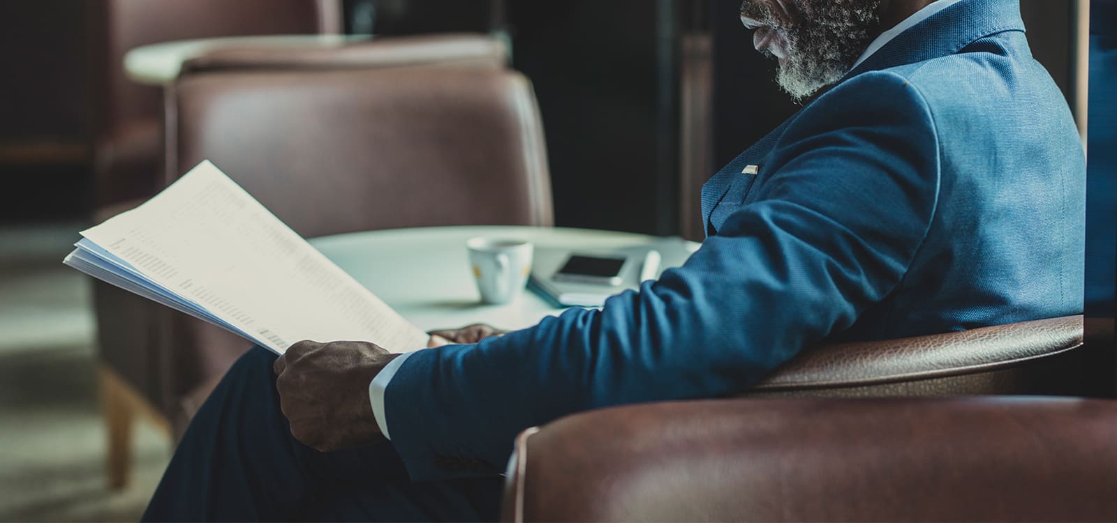 business man in suit sitting in armchair reading paper