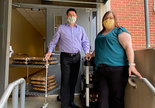man and woman in masks delivering cookies to hospital