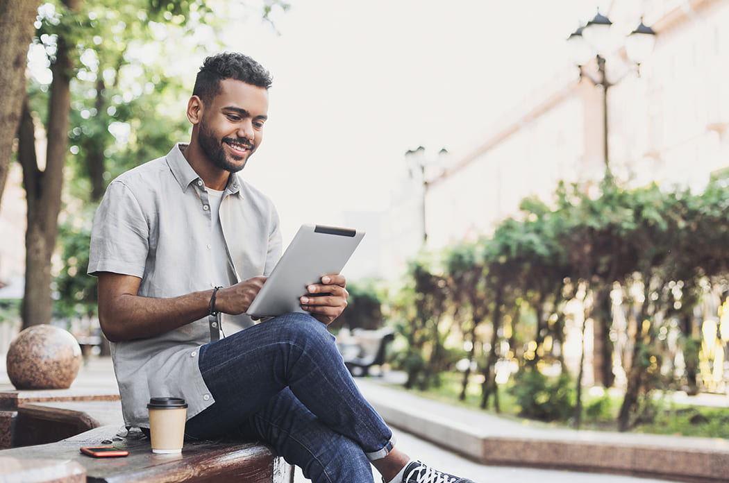 man outdoors with coffee on tablet